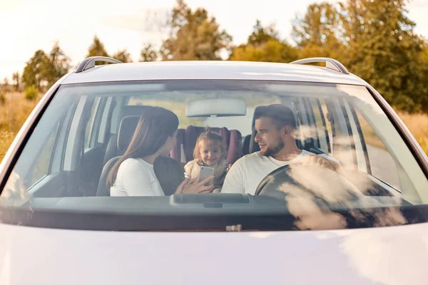 Family, transport, safety, road trip and people. portrait of happy man and woman with little child driving in car, traveling together, mother showing cell phone to child.