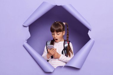 Vay canına, güzel mobil uygulama. Sırt çantası takan, cep telefonu kullanan, ağzı açık alet ekranına bakan, mor kağıt delikte poz veren heyecanlı beyaz kız portresi..