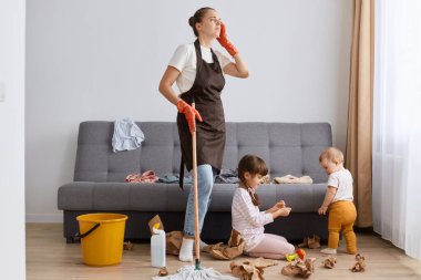 Umutsuzluk portresi. Kahverengi önlüklü yorgun bir kadın. Saç stili, paspas, çocuklarıyla evde temizlik, ev işleri, baş ağrısı, yorgunluk..