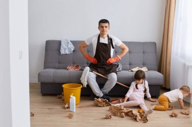 Kahverengi önlük giyen esmer adamın uzun bir portresi. Kanepede oturuyor, ev işlerini yapıyor, daireyi temizliyor. Pisliği temizlemeye nereden başlayacağımı bilmiyorum..