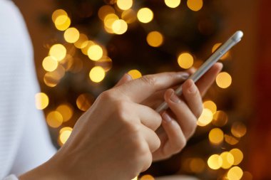 Bilinmeyen bir kadın cep telefonu tutuyor, daktilo yazıyor, arkadaşlarıyla mesajlaşıyor, internette geziniyor, arka planda bulanık Noel ağacıyla akıllı telefonuyla poz veren isimsiz bir kadın..