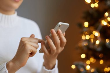 Noel ağacının yanında beyaz kazak giyen, akıllı telefon tutan, sosyal ağları kontrol eden, cep telefonuyla yazı yazan, internet iletişimi için cep telefonu kullanan yüzü olmayan bir kadının portresi..