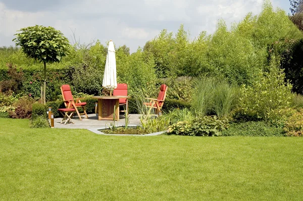 Stół z krzesłami i parasolem, w bujnym ogrodzie — Zdjęcie stockowe