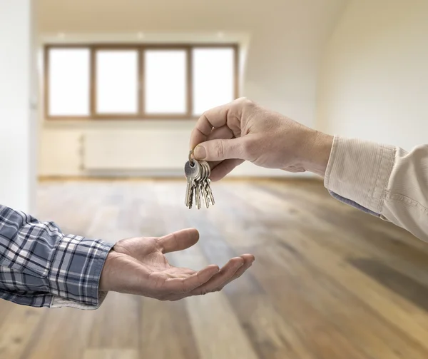 Realtor dando a chave da casa ao comprador no quarto vazio — Fotografia de Stock