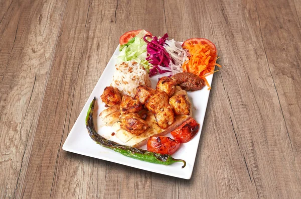 White plate with chicken kebab and vegetables on wooden table