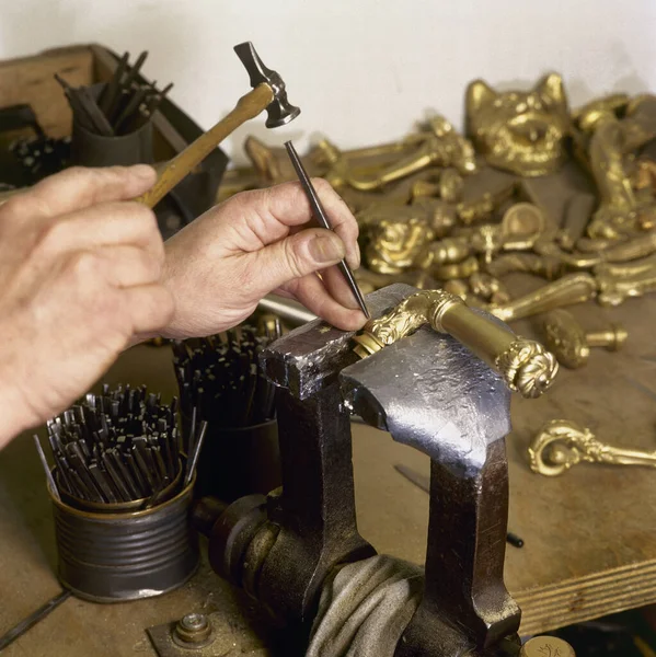 The hands of a craftsman repairs a gold door handle