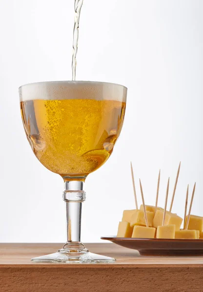 Glass of sparkling Belgian beer with cheese on white background