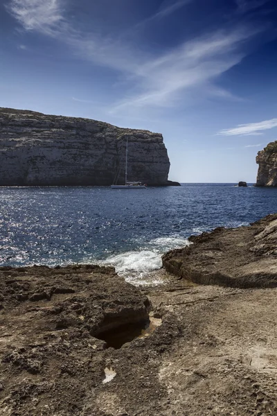 Malta island, gozo, dweira lagune, weergave van een zeilboot en de rotsachtige kustlijn in de buurt van de azuurblauwe venster rots — Stockfoto