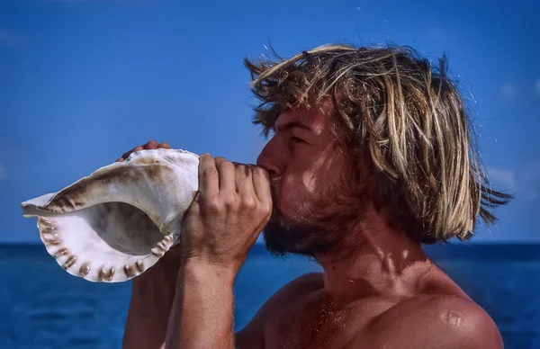 Young man blowing in a seashell — Stock Photo, Image