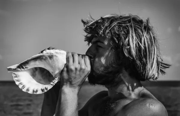 Young man blowing in a seashell — Stock Photo, Image