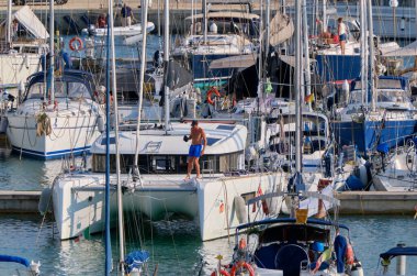 İtalya, Sicilya, Akdeniz, Marina di Ragusa (Ragusa Eyaleti); 30 Eylül 2021, limandaki bir yelkenli ve lüks yatlarda bir adam - EDITORIAL