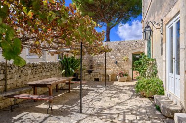 İtalya, Sicilya, Modica (Ragusa Eyaleti), kırsal kesim, masa ve eski bir taş evin koltukları ile yan avlu 