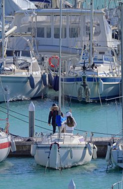 İtalya, Sicilya, Akdeniz, Marina di Ragusa (Ragusa ili); 4 Aralık 2021, limandaki insanlar ve yelkenliler - EDITORIAL