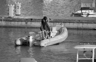 İtalya, Sicilya, Akdeniz, Marina di Ragusa (Ragusa Eyaleti); 19 Nisan 2022, limanda kauçuk bir tekne ve lüks yatlarda bir çift - EDITORIAL