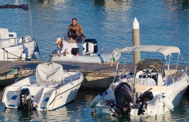 İtalya, Sicilya, Akdeniz, Marina di Ragusa (Ragusa Eyaleti); 15 Temmuz 2022, limanda kauçuk bir tekne ve lüks yatlarda bir çift - EDITORIAL