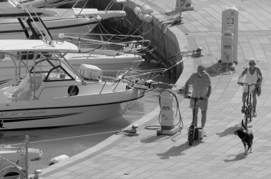 İtalya, Sicilya, Akdeniz, Marina di Ragusa (Ragusa Eyaleti); 1 Ekim 2022, limanda köpekleri ve lüks yatlarıyla bisiklet süren çift - EDITORIAL