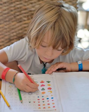 6 yaşındaki erkek çocuk ödevini evde bir masada yapıyor.