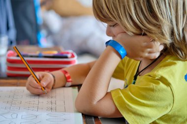 6 yaşındaki erkek çocuk ödevini evde bir masada yapıyor.