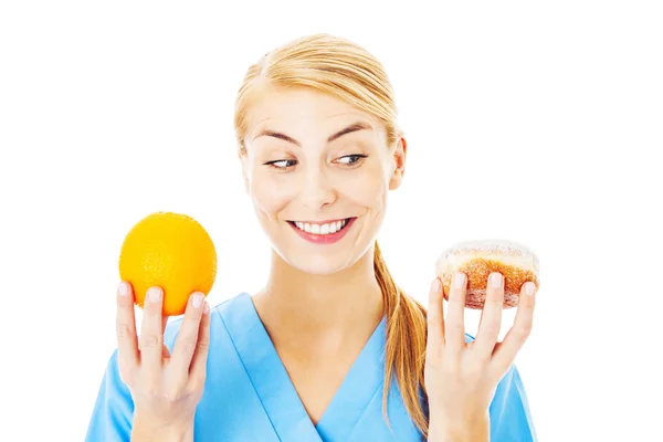 Медсестра держит сладкую еду и апельсин на белом фоне — стоковое фото