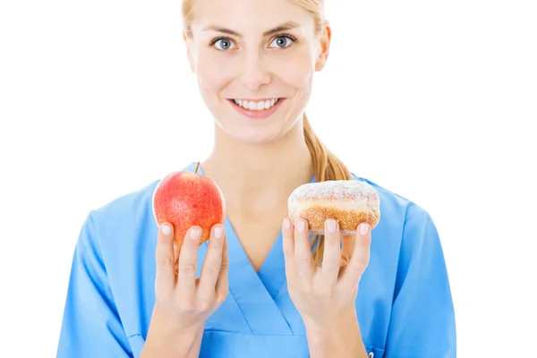 Sjuksköterska hålla söt mat och apple över vit bakgrund — Stockfoto