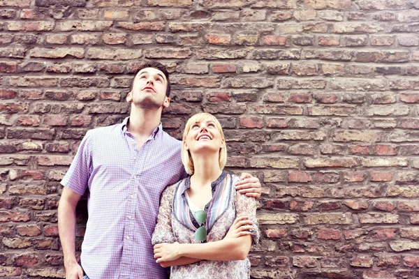 Pareja joven mirando contra la pared de ladrillo —  Fotos de Stock