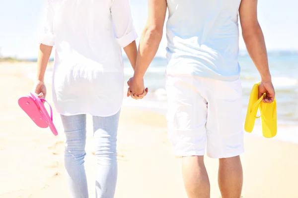 Pareja caminando en la playa y llevando chanclas — Foto de Stock