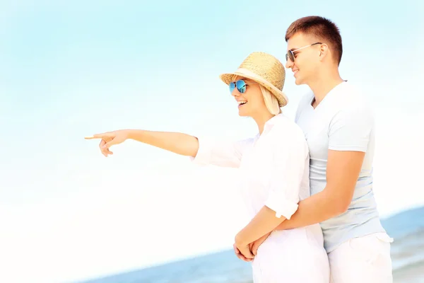 Lyckliga paret kramas på stranden och pekar — Stockfoto