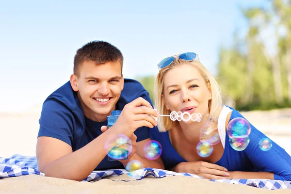 Giovane coppia soffia bolle in spiaggia — Foto Stock