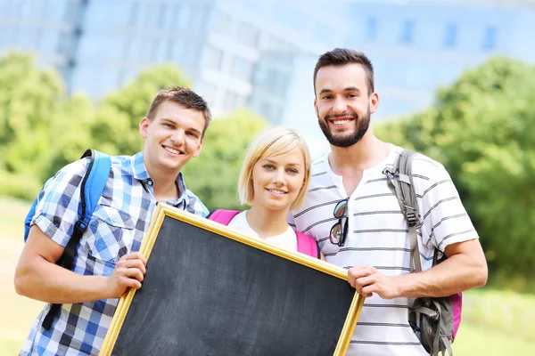 Group of students holding a blackboard in the park — Stock Photo, Image
