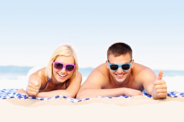 Happy couple sunbathing at the beach clipart