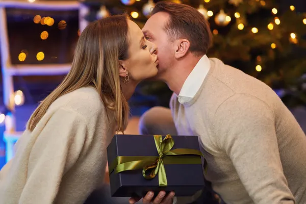 Couple giving christmas gift in front of a tree — Stock Photo, Image