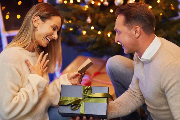 Casal dando presente de Natal na frente de uma árvore — Fotografia de Stock
