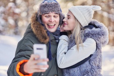 Genç çift karla eğleniyor ve selfie çekiyor.