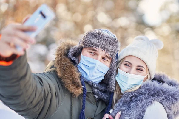 Mladý pár baví na sněhu přičemž selfie na sobě masku — Stock fotografie