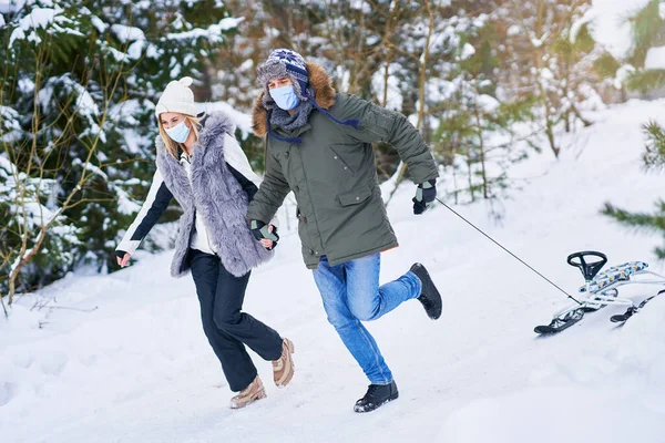 Couple having fun with sledge on snow wearing mask — Stock Photo, Image