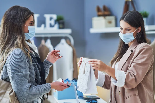 Női eladó és vevő a ruhaboltban maszkot visel — Stock Fotó