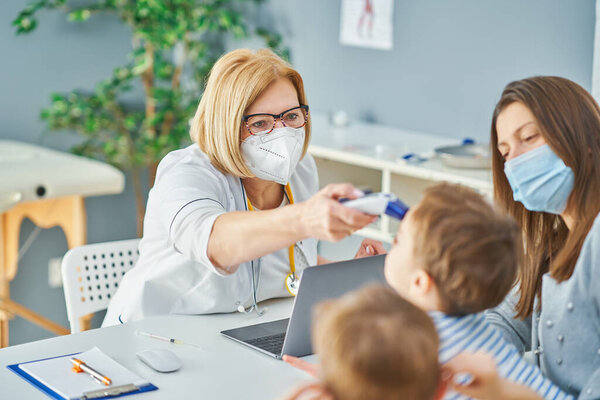 Врач-педиатр осматривает маленьких детей в клинике