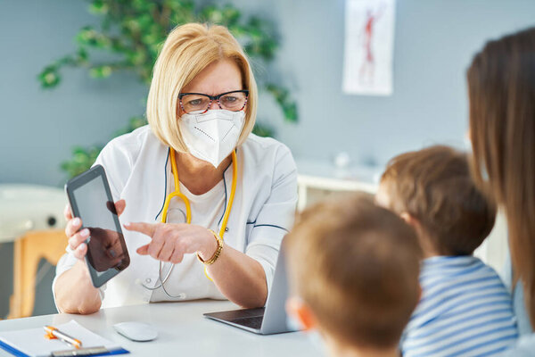 Врач-педиатр осматривает маленьких детей в клинике