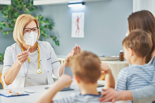 Врач-педиатр осматривает маленьких детей в клинике