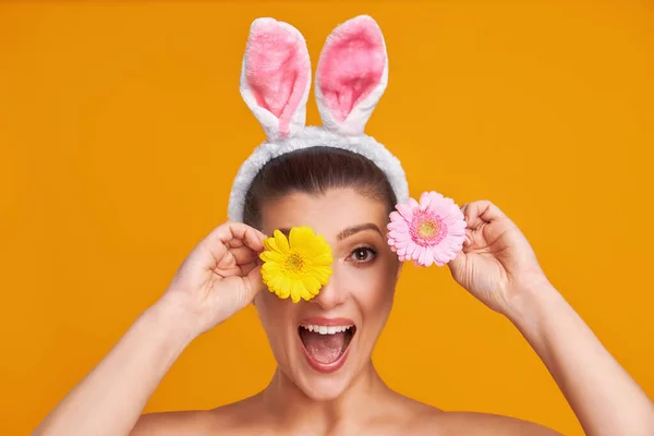 Belle jeune femme sur fond jaune avec des oreilles et des fleurs de Pâques lapin — Photo