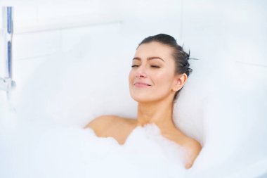 Genç, güzel esmer kadın küvette banyo yapıyor.