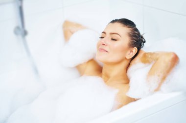 Genç, güzel esmer kadın küvette banyo yapıyor.