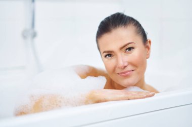 Genç, güzel esmer kadın küvette banyo yapıyor.