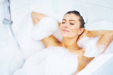 Genç, güzel esmer kadın küvette banyo yapıyor.