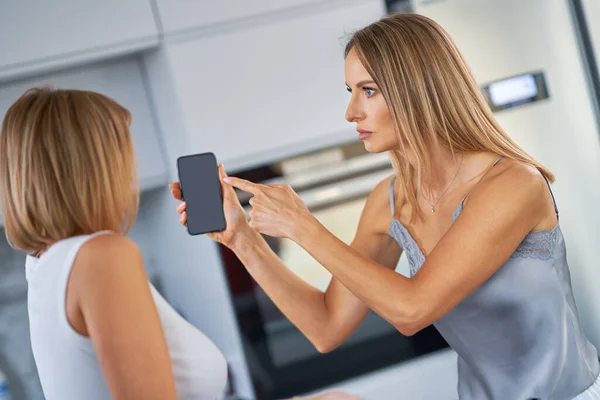 Хороші дві дорослі дівчата в хаті сперечаються з мобільним телефоном — стокове фото