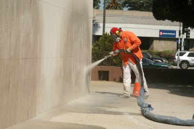 An unidentifiable city worker sand blast away graffiti on a wall clipart