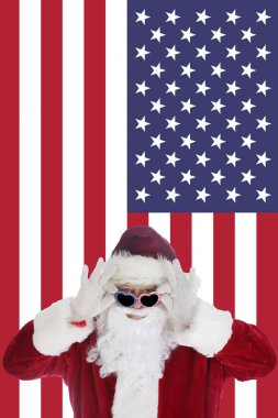 Noel Baba, Amerikan Bayrak Arkaplanı ile güneş gözlüğünü takarken gülümsüyor. Mutlu Noeller ve mutlu tatiller. Mutlu Noeller ve mutlu yıllar. Amerikan bayrağının önünde Noel Baba 'nın olduğu tebrik kartı. Kış tatilleri. Ho Ho Ho.