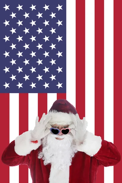 圣诞老人笑着戴上印有美国国旗背景的太阳镜 圣诞快乐 节日快乐 圣诞快乐 新年快乐 圣诞老公公坐在美国国旗前的贺卡 何浩浩 — 图库照片