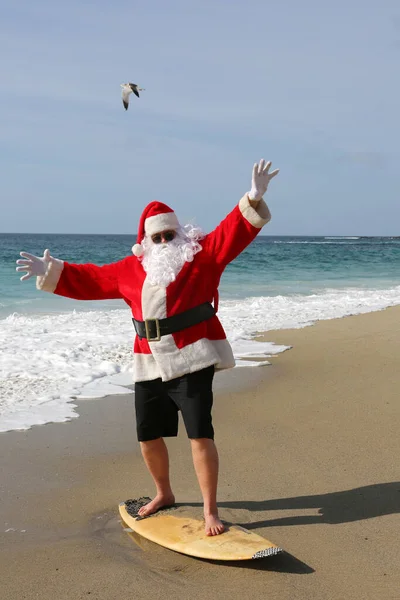 冲浪圣诞老人 圣诞老人骑的是冲浪板 戴着太阳镜的圣诞老人在海里冲浪 圣诞老人在他的冲浪板上冲浪 而在美丽的海滩与蓝色的海洋 圣诞假期 — 图库照片