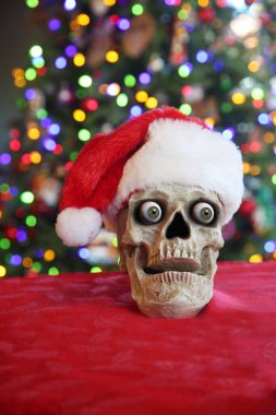 Noel Kafatası. Noel Baba şapkası takan ürkütücü bir insan kafatası. Noel ağacının önündeki insan kafatası. Mutlu noeller. Lanetli Noel. Noel Zombisi. 